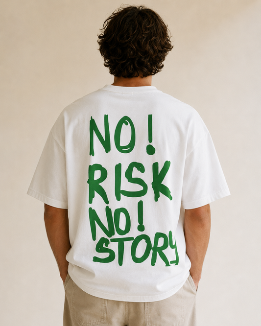 Back view of a white T-shirt with large green graffiti-style text reading ‘NO! RISK NO! STORY!’