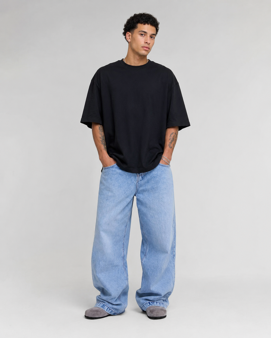A man modeling an oversized black short-sleeve t-shirt and light-wash wide-leg blue jeans against a plain light gray studio background.