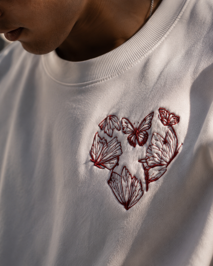 White sweatshirt with red butterfly embroidery on a neutral background