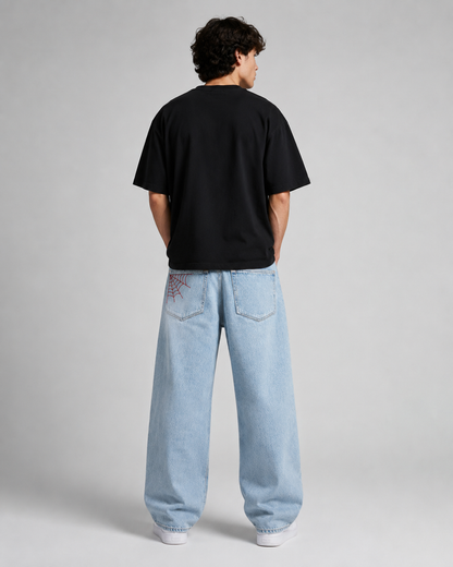 A model shown from the back wearing a black t-shirt and light-wash wide-leg jeans, standing against a neutral gray studio background.