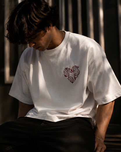 Person wearing a white t-shirt with a red and black design, sitting outdoors.
