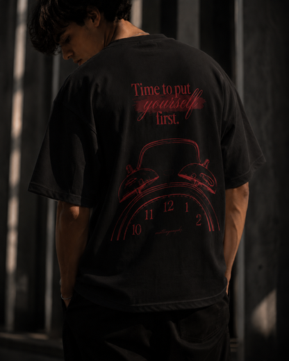 Person wearing a black t-shirt with red text and design on the back, standing against a dark background.