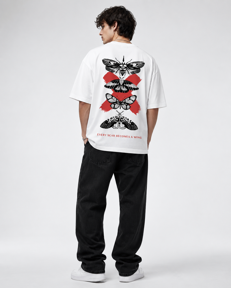 A man viewed from behind wearing a white t-shirt with a large red and black moth graphic on the back, paired with black jeans and white sneakers, against a light gray studio background.